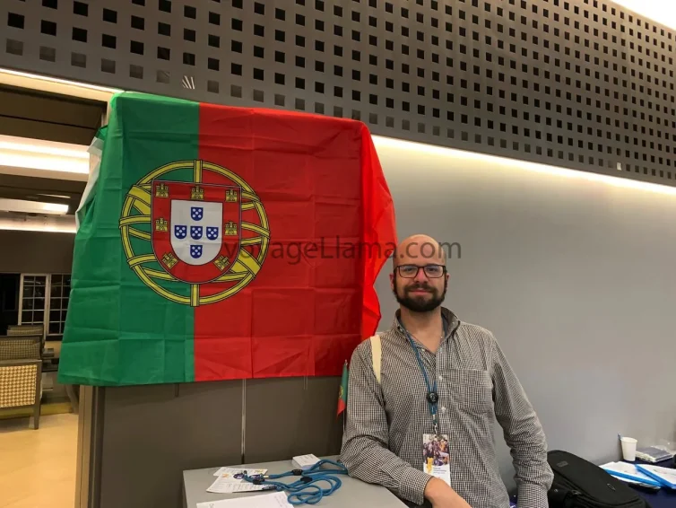 Hombre sentado junto a una bandera de Portugal en un recinto interior.