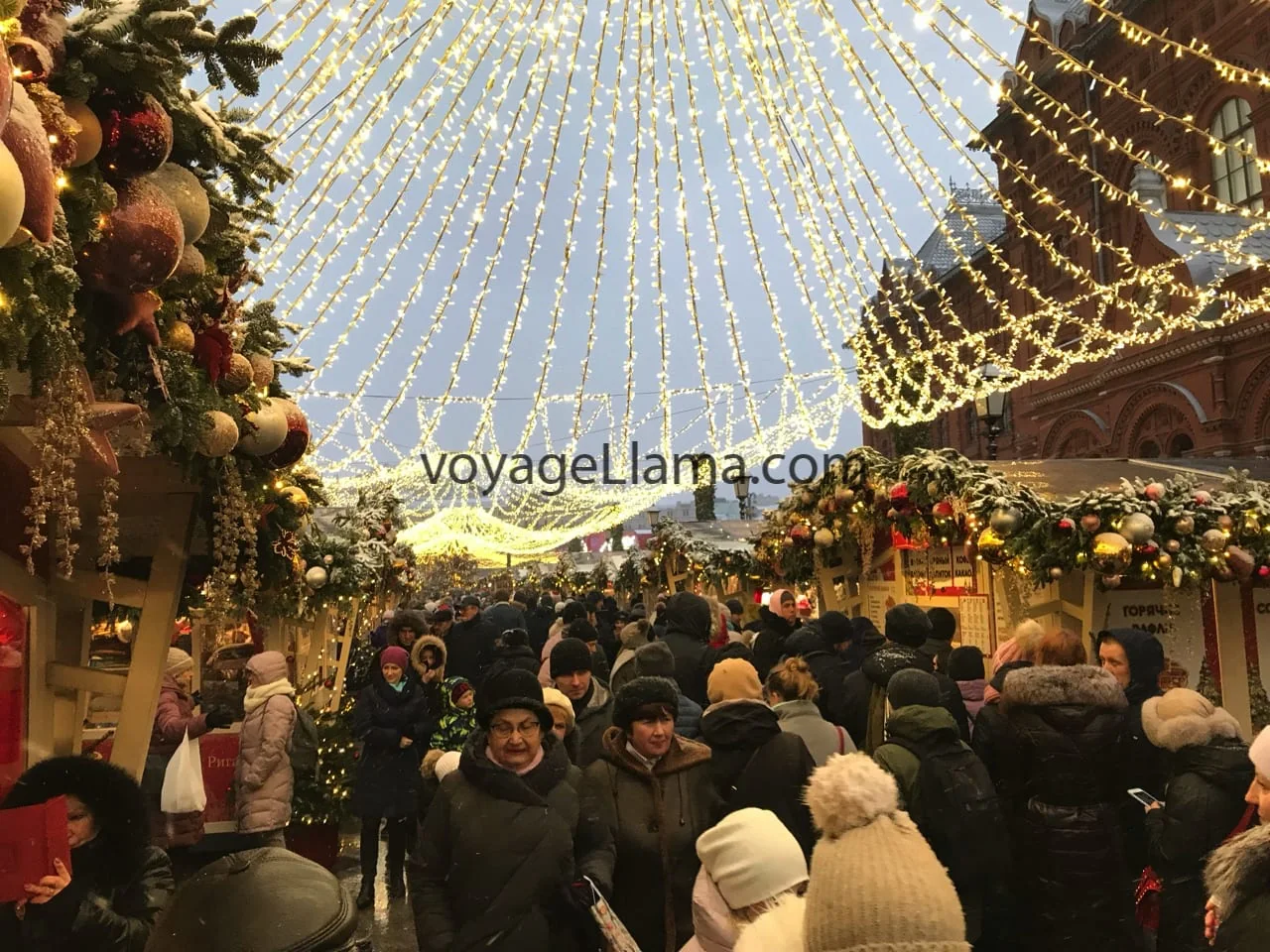 Mercado navideño iluminado y lleno de visitantes.