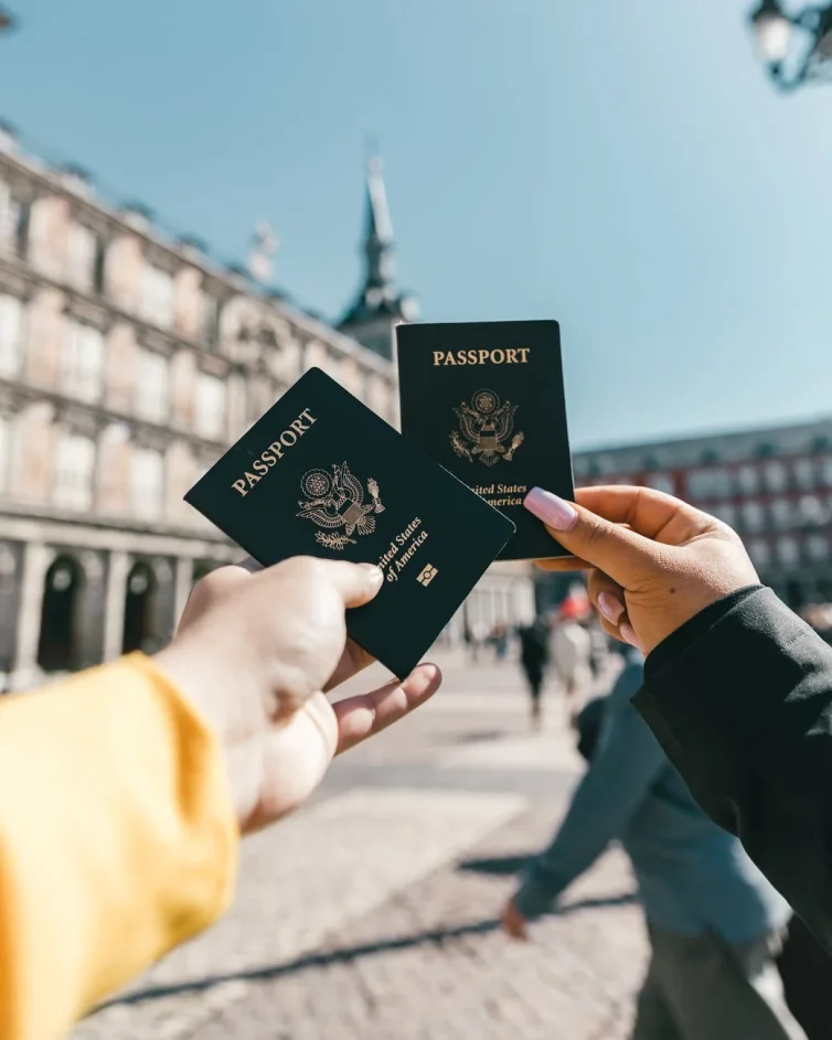 Dos pasaportes de Estados Unidos de América sostenidos frente a una plaza.