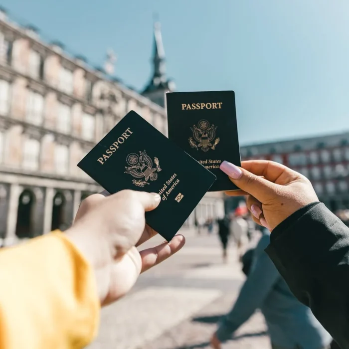 Dos pasaportes de Estados Unidos de América sostenidos frente a una plaza.