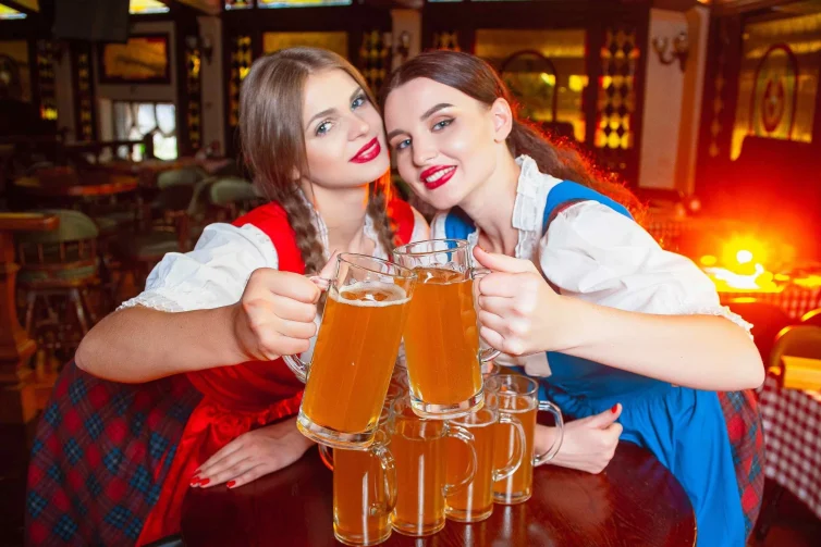 Dos mujeres con vestimenta tradicional alemana brindando con cerveza.