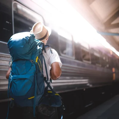 Viajero con mochila junto a un tren en una estación.