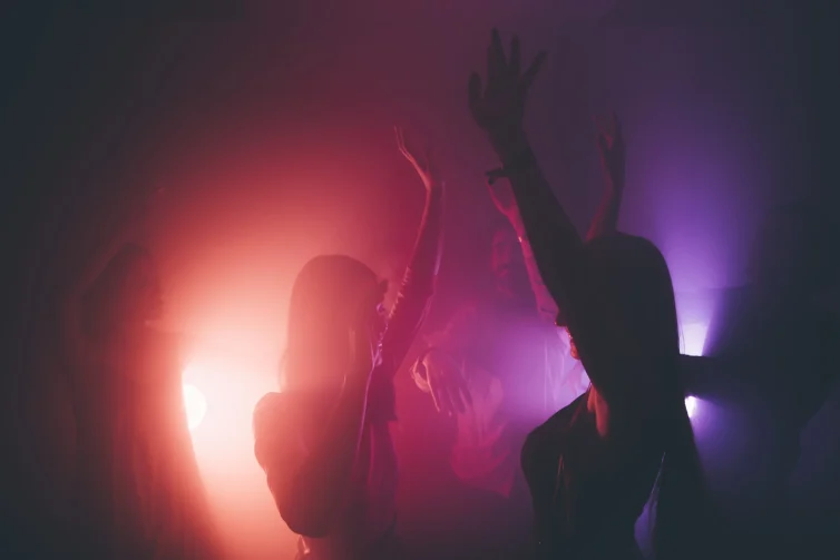 Siluetas de personas bailando bajo luces de una discoteca.